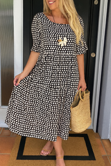 Robe midi élégante à pois de la marque Olyndra London, tissu fluide et coupe sophistiquée, portée avec accessoires.